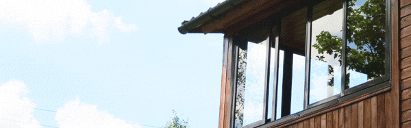 На балконе - веранде дачного дома установлены раздвижные окна коричневого цвета. Недорого и удобно.