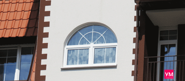 Арочное белое окно со шпросами внутри стеклопакета. Установлено в малоэтажном доме.