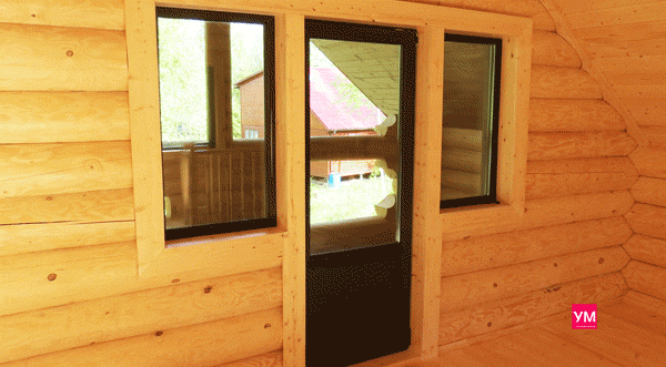 Коричневые окна из пластика в доме из бревна. Вид изнутри помещения. Выход на террасу.