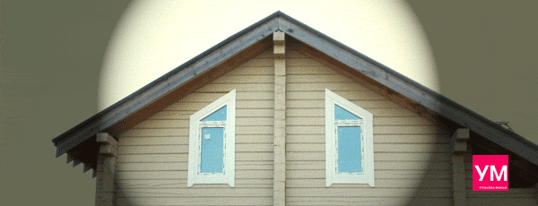 Два трапециевидных окна белого цвета установлены под скатами крыши дома из профилированного бруса